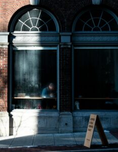 Facade of house with unrecognizable man sitting behind arched window in cafe located on narrow pathway in city street in daylight